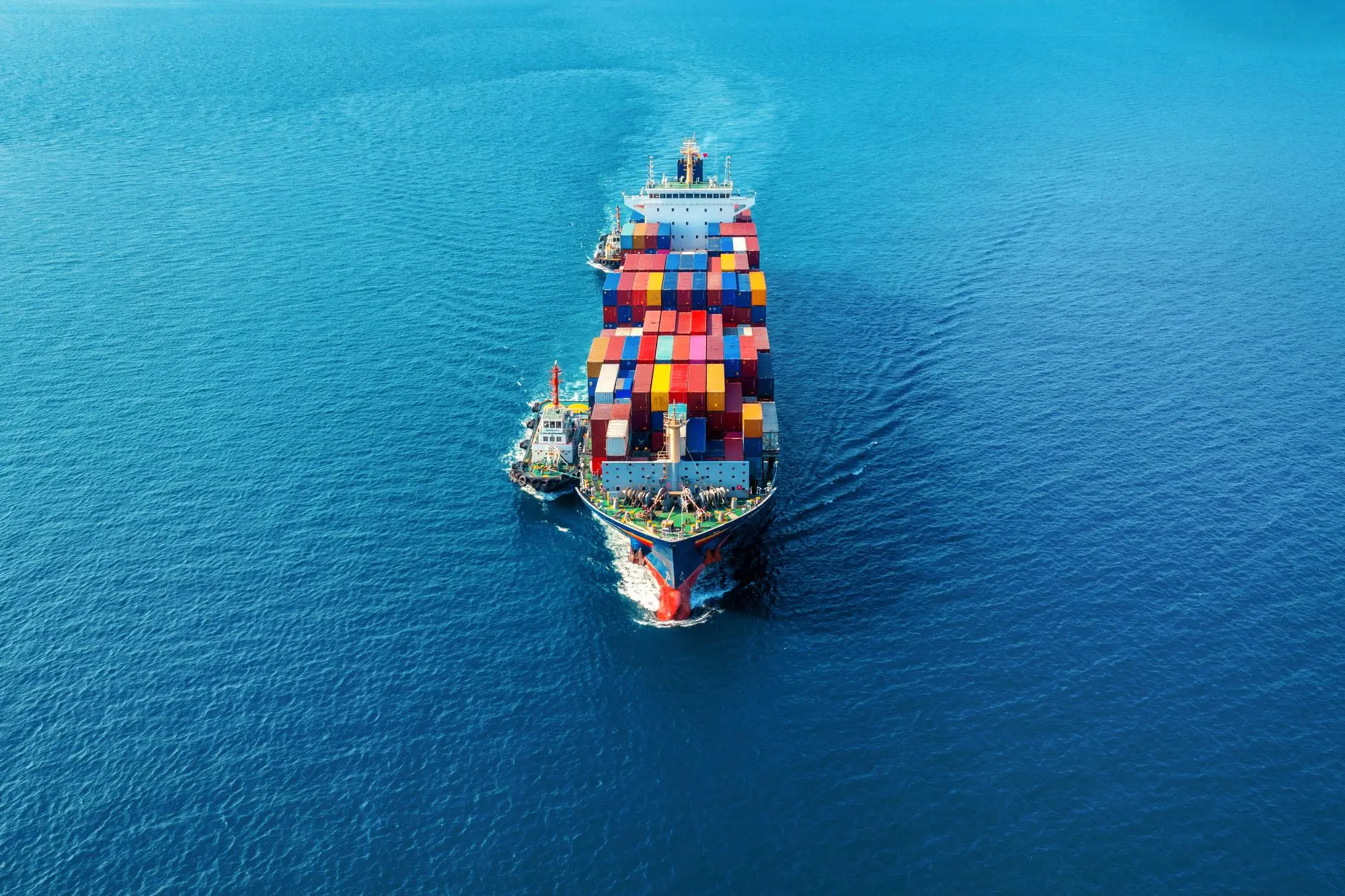 Aerial view of a loaded container ship at sea with tugboats alongside