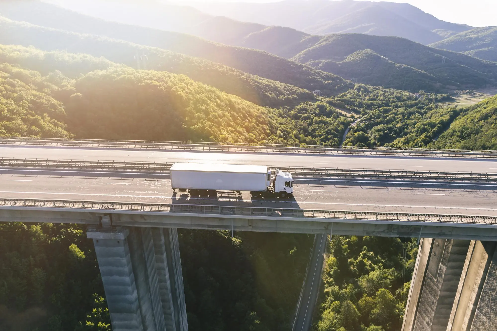 Articulated lorry crossing a motorway viaduct through wooded hills