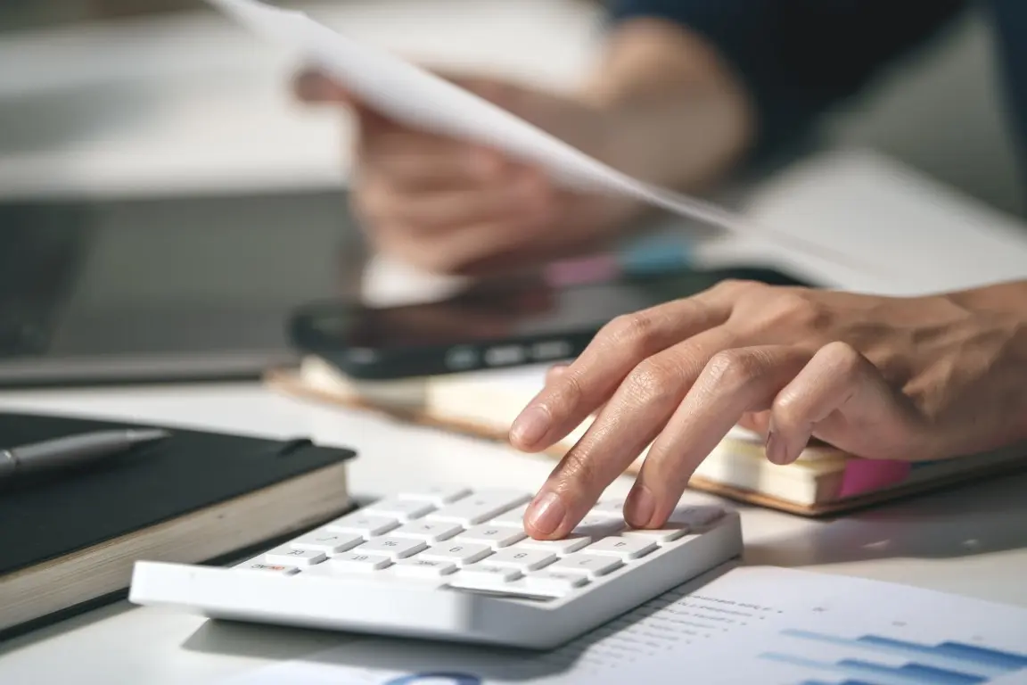 Hand pressing keys on a desk calculator next to financial documents.